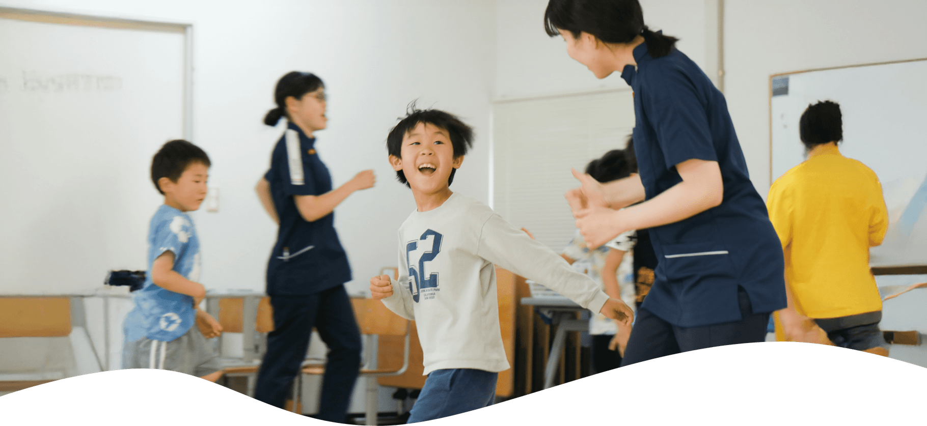 教室のような場所でかけっこをする先生と子どもたち