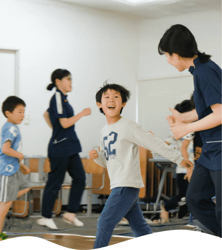 教室のような場所でかけっこをする先生と子どもたち