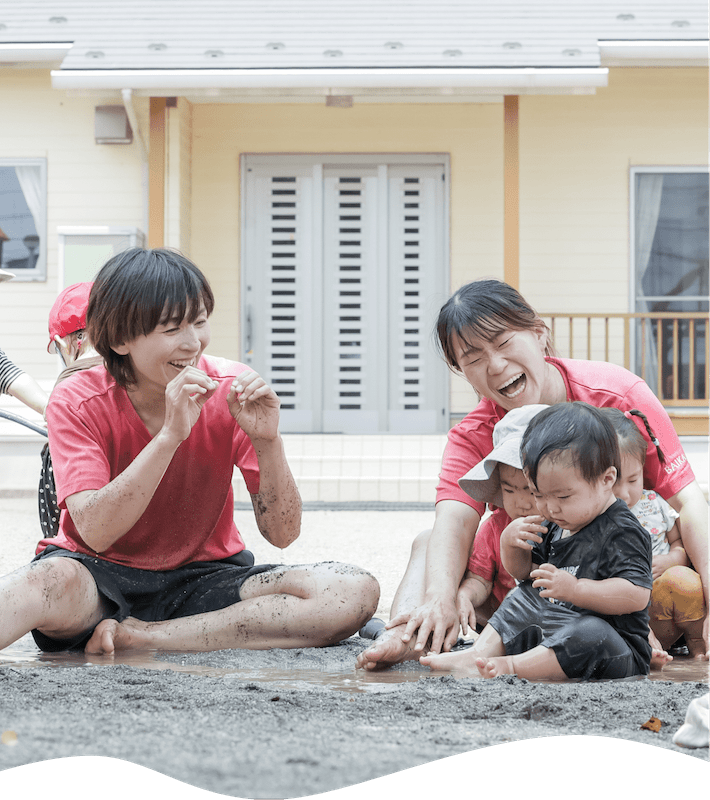 泥で遊ぶ子ども達と2人の先生
